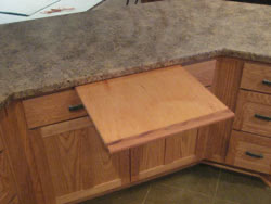 A pullout cutting board in a cabinet with a brown granite top