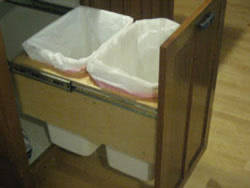 An open drawer with a garbage can and recycling can