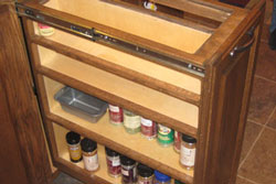 An pullout spice rack in a kitchen with dark brown tiles