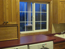 A laundry room with red counters and light wood cabinets