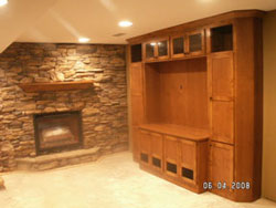 A stone wall with a floating wood mantle over a fireplace